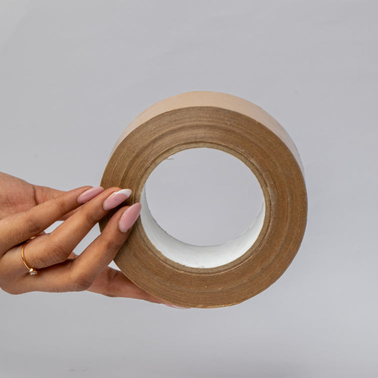 Hands applying eco-friendly tapes to a cardboard material for secure packaging.			